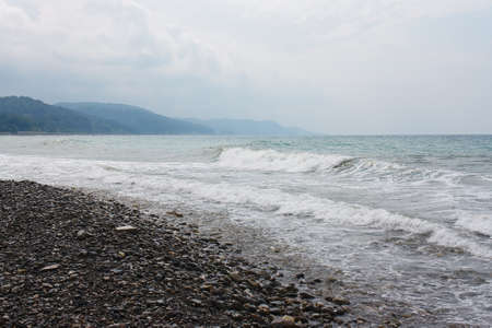 Sea waves on the beach against the cloudy sky of the mountainous coastの写真素材