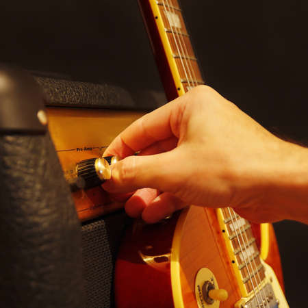 Hand adjusts amplifier for guitar with electric guitar on the black background. Shallow depth of...