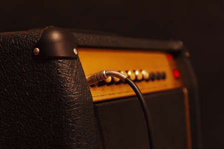 Combo amplifier for electric guitar with inserted input jack on the black background. Shallow depth...