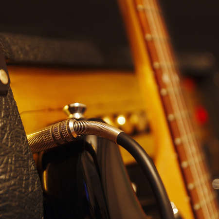 Input jack inserted to amplifier for electric guitar with guitar on the black background. Shallow depth of field, low key, close up. Focus on input jack.の写真素材