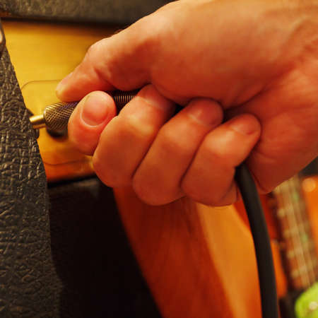 Hand inserts input jack to combo amplifier for guitar. Shallow depth of field, low key, close up.の写真素材