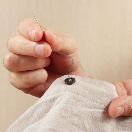 Hands of tailor sew a button to cotton fabric close up