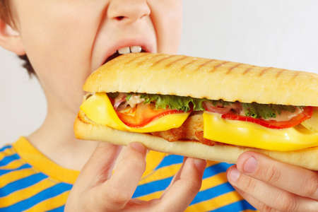 Little cut boy eating a tasty cheeseburger on a white background close upの写真素材