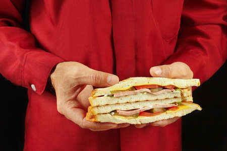 Hands of man in a red shirt are holding a double sandwich on a black backgroundの写真素材