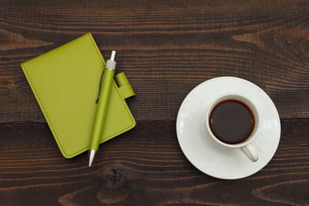 Cup of coffee, pen and green notebook on a wooden background. View from above.の写真素材