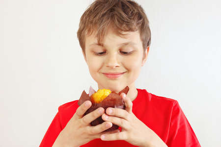Young cut boy in a red shirt eating muffin on a white background.の写真素材