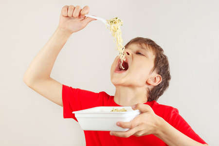 Young cut boy in a red shirt eating instant noodles on a white background.の写真素材