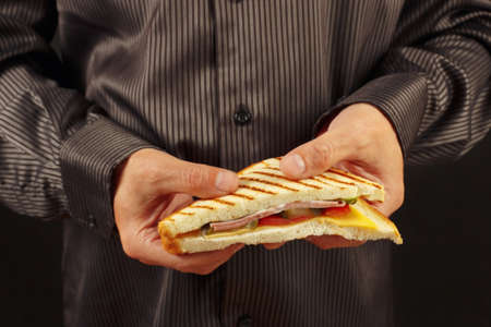 Hands of man in a black shirt are holding a sandwich on a black background close upの写真素材