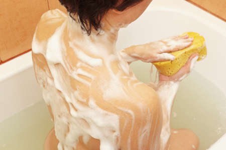 Attractive woman with soaped sponge in the bathroom close up