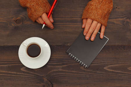 Hands of writer with a pen and notebook at a wooden table with a cup of coffeeの写真素材