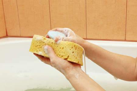 Hands of woman soaping a yellow sponge in the bathroom