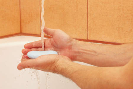 Hands of man with soap under the water in the bathroom