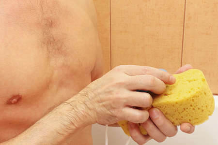 Handsome young man soaping a yellow sponge with soapの写真素材