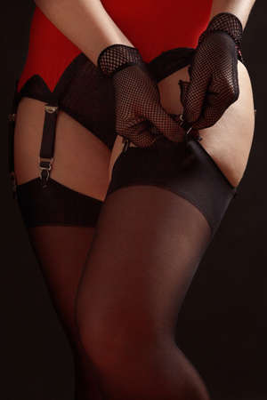 Woman fastens black stockings to the erotic garter belt on a black background close upの写真素材