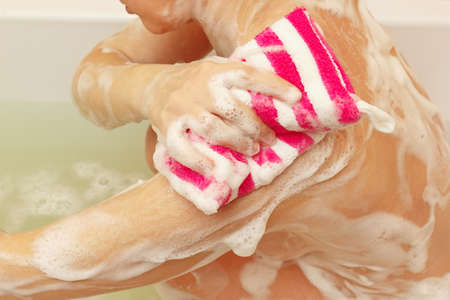 Attractive woman lathering sponge shoulder in the bathroom close upの写真素材