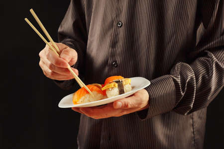 Hands of man in a black shirt with plate with sushi and rolls on a black backgroundの写真素材