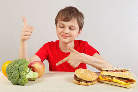 Young boy at the table chooses between fastfood and healthy diet on a white background