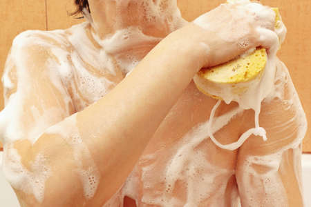 Beautiful young woman lathering sponge shoulder in the bathroom close up