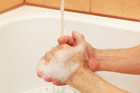 Man`s hands with soap under the jet of water in the bathroom
