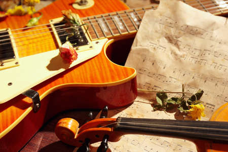 Vintage electric guitar, rare violin, dried flowers and old sheet music on wooden background close...