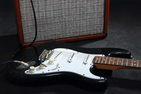 Brown amplifier for electric guitar with black guitar on the black background.