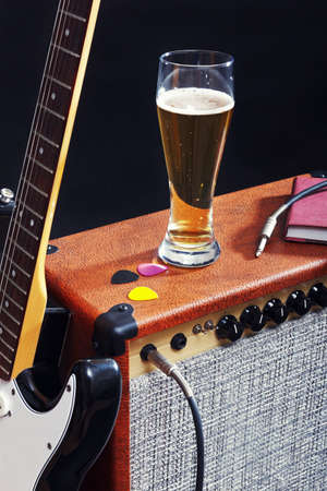 Tube combo for electric guitar with black guitar, glass of beer and notepad on the black background.の写真素材