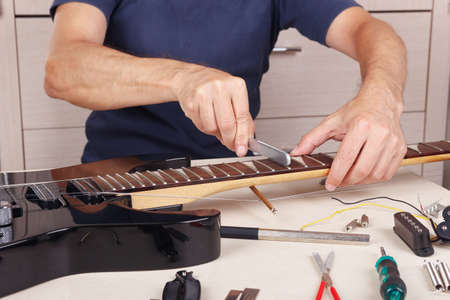 Guitar master crowning frets on the electric guitar neck with fret files.