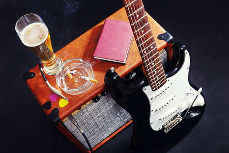 Tube combo amplifier for electric guitar with black guitar, glass of beer and smoking cigarette on the black background.の写真素材