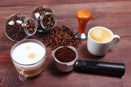 Cups of espresso and cappuccino, holder with ground coffee, tamper and coffee beans on the table.の写真素材