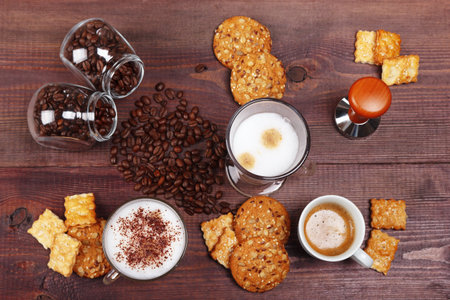 Cups of espresso, latte and cappuccino, crackers, holder with ground coffee, tamper and coffee beans on the wooden table. view from above.の写真素材