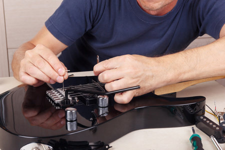 Guitar repairer adjusts the tremolo bridge on modern electric guitar.の写真素材
