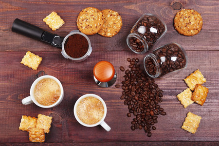 Two cups of espresso, crackers, holder with ground coffee, tamper and cans of coffee beans on the wooden table. view from above.の写真素材