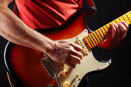 Guitarist in red plays the sunburst electric guitar on a dark stage.の写真素材