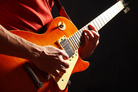 Rock musician in red plays the orange electric guitar on a dark stage.の写真素材