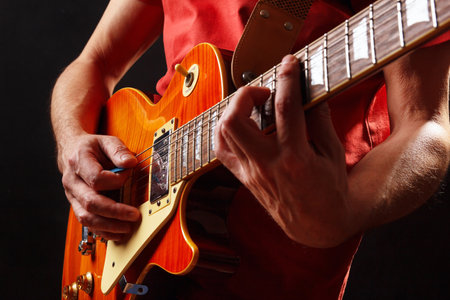 Guitarist in red plays the orange electric guitar on a dark stage.の写真素材