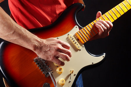 Rock guitarist in red plays the sunburst electric guitar on a dark stage.の写真素材