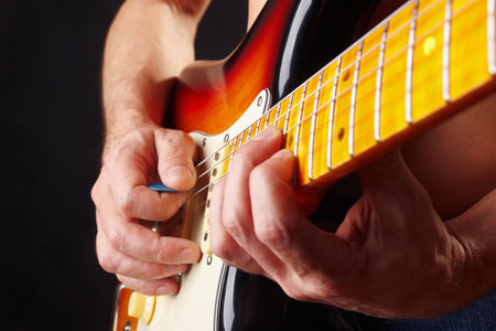 Hands of guitarist playing the sunburst guitar on a dark stage.の写真素材