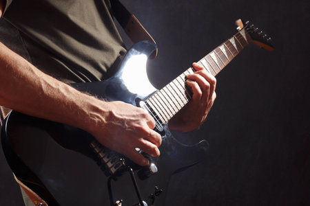 Posing hands of rock musician playing the black guitar on a dark stage.の写真素材
