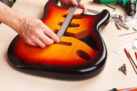 Guitar repairman measures body of guitar with a ruler.の写真素材