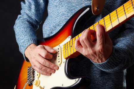 Artist in blue sweater plays the sunburst electric guitar on a dark stage.の写真素材