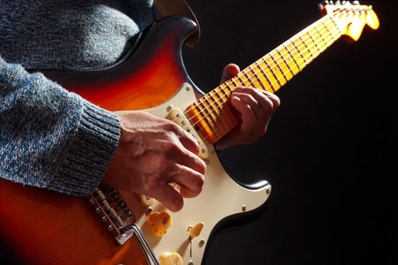 Musician in blue sweater plays the sunburst electric guitar on a dark stage.の写真素材