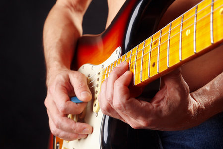 Hands of rock guitarist playing the sunburst guitar on a dark stage.の写真素材
