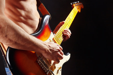 Musician playing the sunburst electric guitar on a dark stage.の写真素材