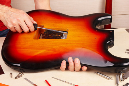 Guitar technician screws the holder of tremolo springs in the guitar body.の写真素材