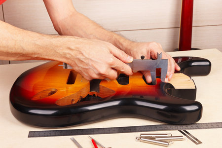 Guitar technician measures body of guitar with a caliper.の写真素材