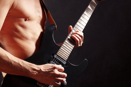 Artist playing chord on black guitar on a dark stage.の写真素材
