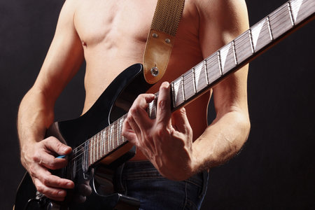 Hands of rock musician with black guitar on a dark stage.の写真素材