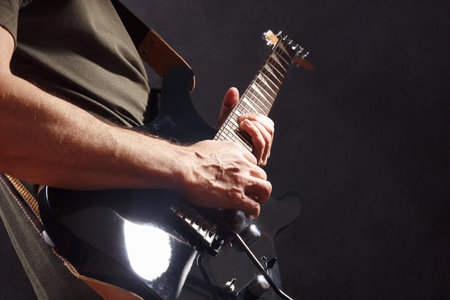 Hands of guitarist with black guitar on a dark stage.の写真素材