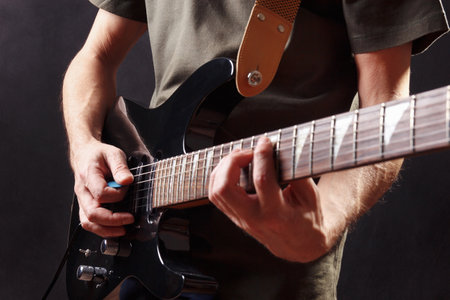 Hands of rock musician playing the black guitar on a dark stage.の写真素材