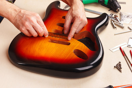 Guitar technician measures size of holes for tremolo in body of guitar with a ruler.の写真素材